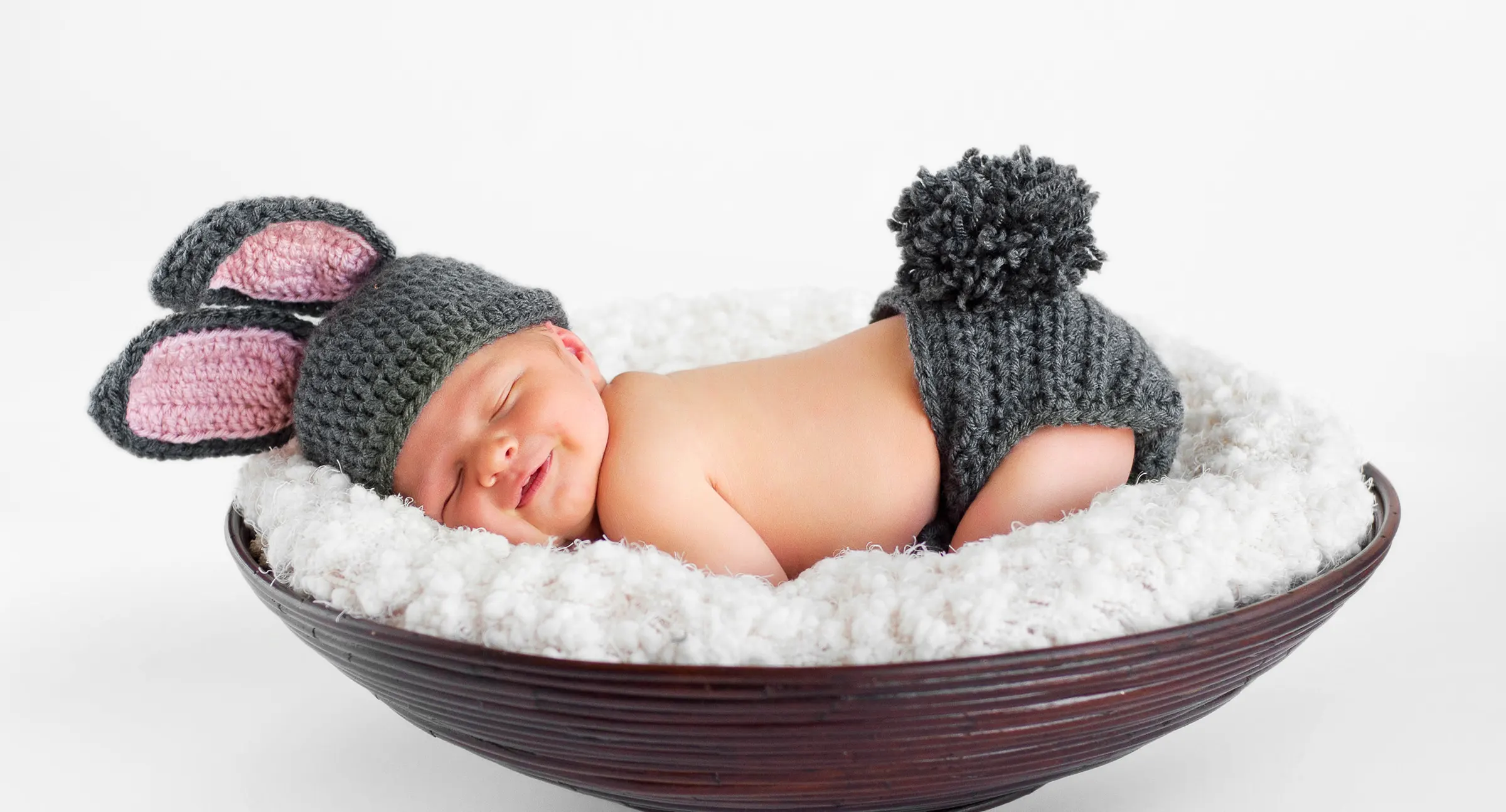 A happy baby laying down with rabbit years hat.